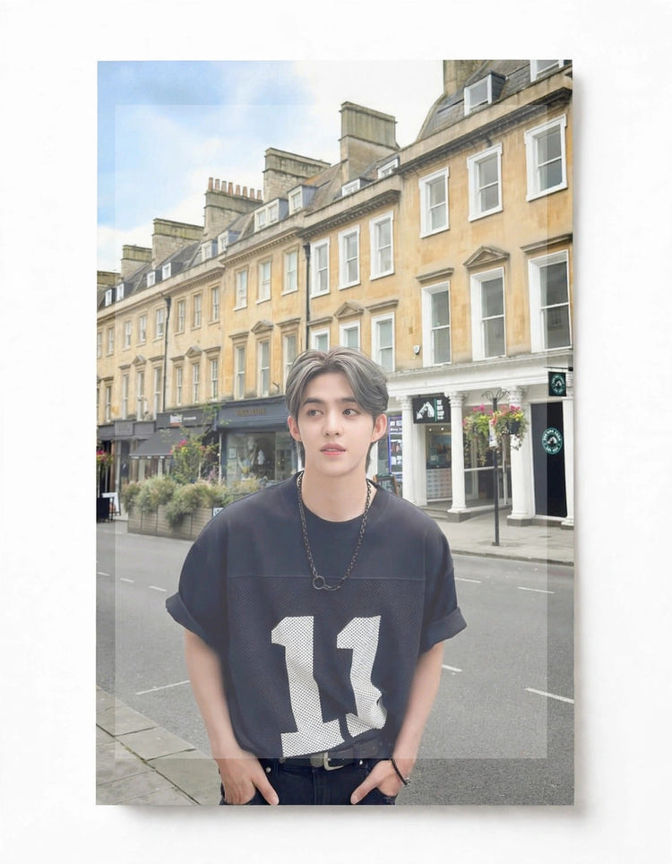 A vertical photo print or poster featuring a young man standing on a city street in front of tan row houses, wearing a dark oversized T-shirt with a large white number 11 on the front. The print is shown against a plain white background with a subtle drop shadow.