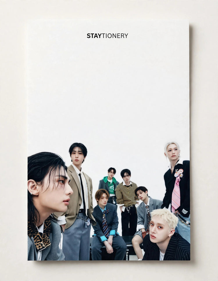 A vertical STAYTIONERY notebook or planner cover photographed against a light beige background. The cover features a group photo of seven young men in stylish outfits, with the brand name 'STAYTIONERY' printed at the top.