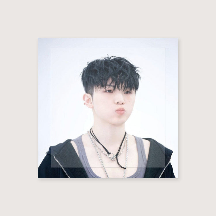 A square instant photo print featuring a portrait of a young man with dark hair, wearing layered silver and black necklaces, a black hoodie, and a gray tank top, set against a plain light background.